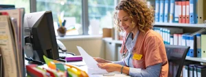 a vibrant office environment showcases a confident medical billing specialist meticulously organizing patient files surrounded by colorful charts and orthopedic equipment, illuminated by soft, natural light streaming through a large window.